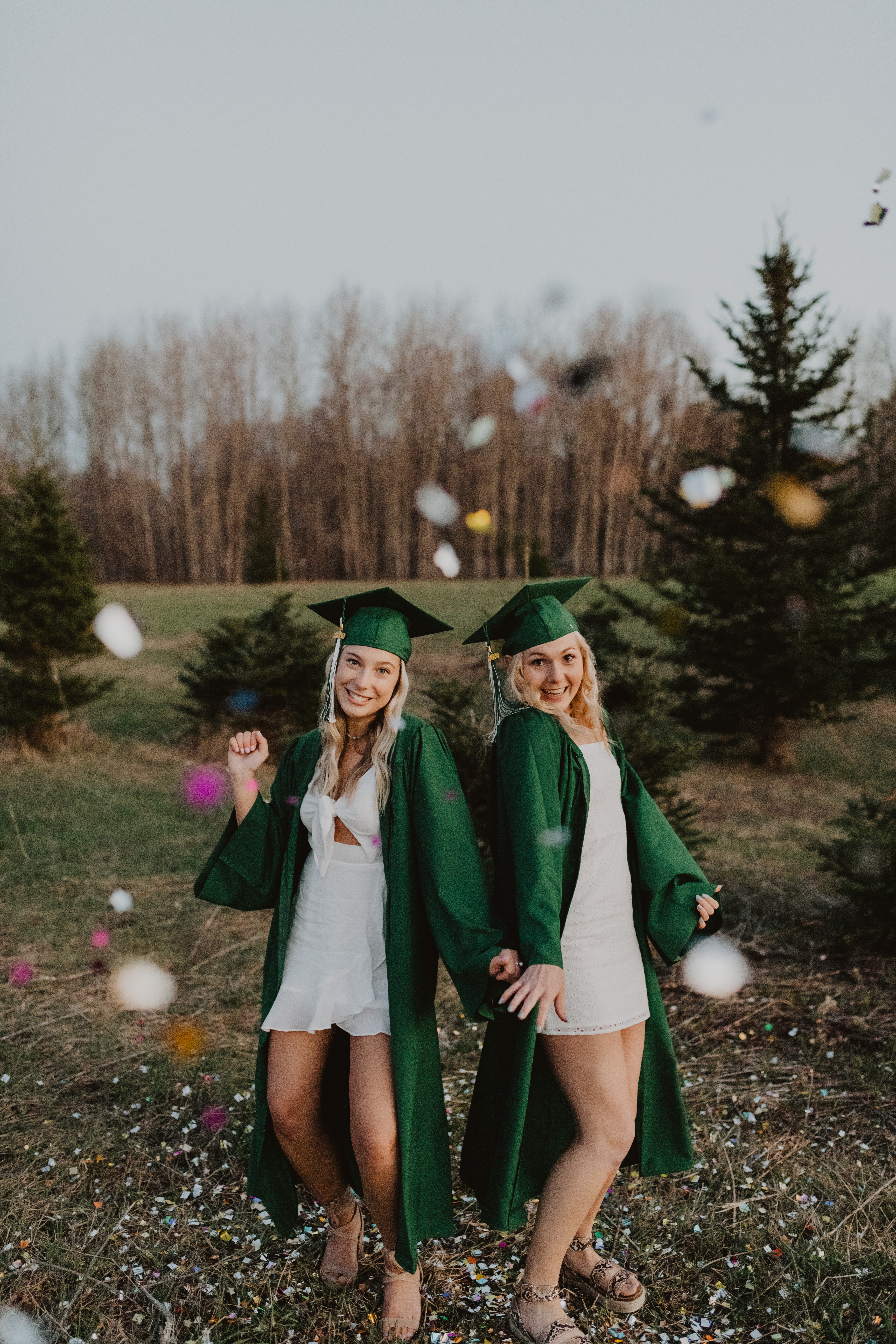 two girls throwing confetti in their graduation cap + gowns