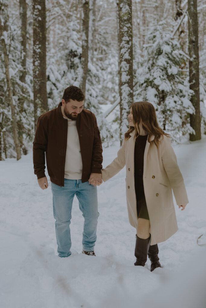 Couple walking hand in hand through the snow during a winter engagement session in Northern Wisconsin
