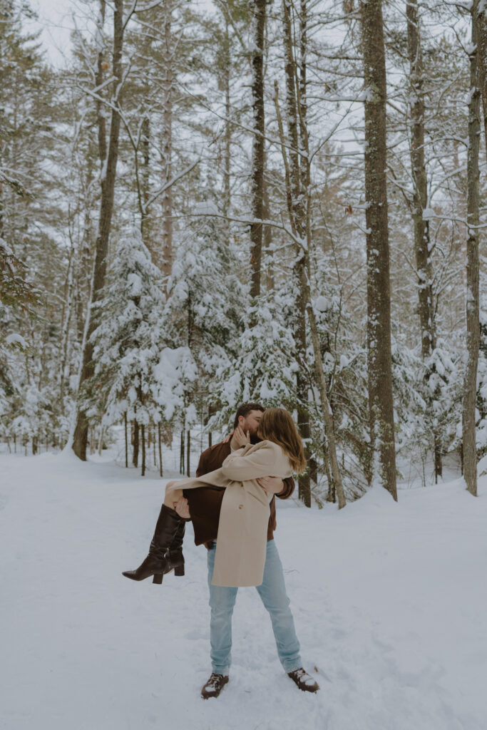 Couple embracing during a winter engagement session among snow-covered pine trees in St. Germain, Wisconsin