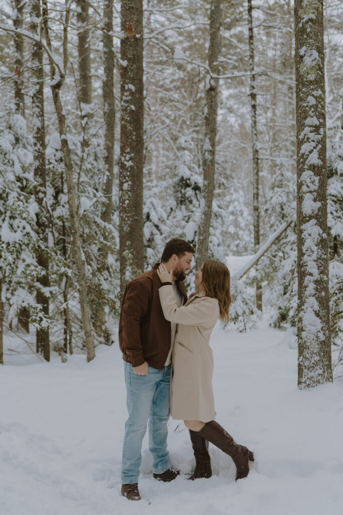 Couple embracing during a winter engagement session among snow-covered pine trees in St. Germain, Wisconsin