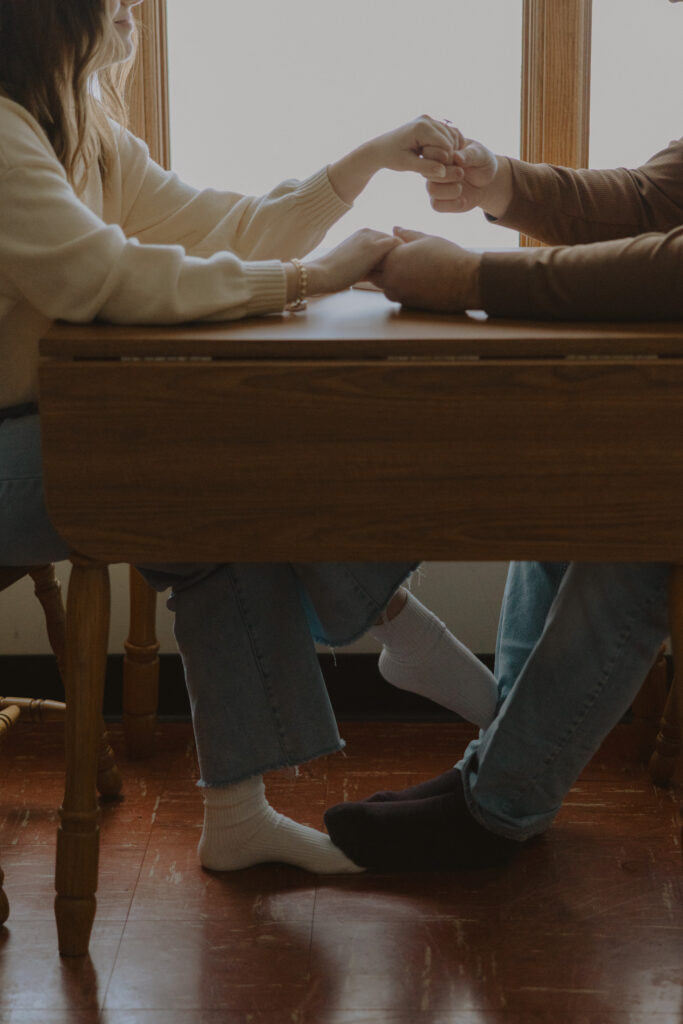 Couple holding hands across a table inside a cozy cabin during a winter engagement session in Northern Wisconsin